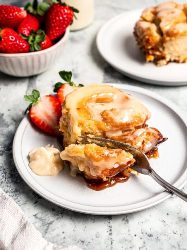 A fork cutting into a caramel roll next to fresh berries on a plate.