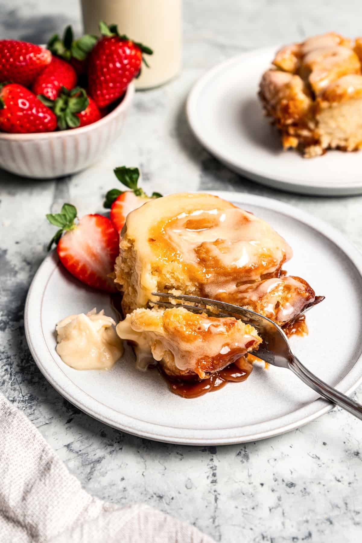 These sweet and gooey homemade caramel rolls require no yeast, rise time, or kneading. They're easy, quick, and best of all, delicious! A fork cutting into a caramel roll next to fresh berries on a plate.