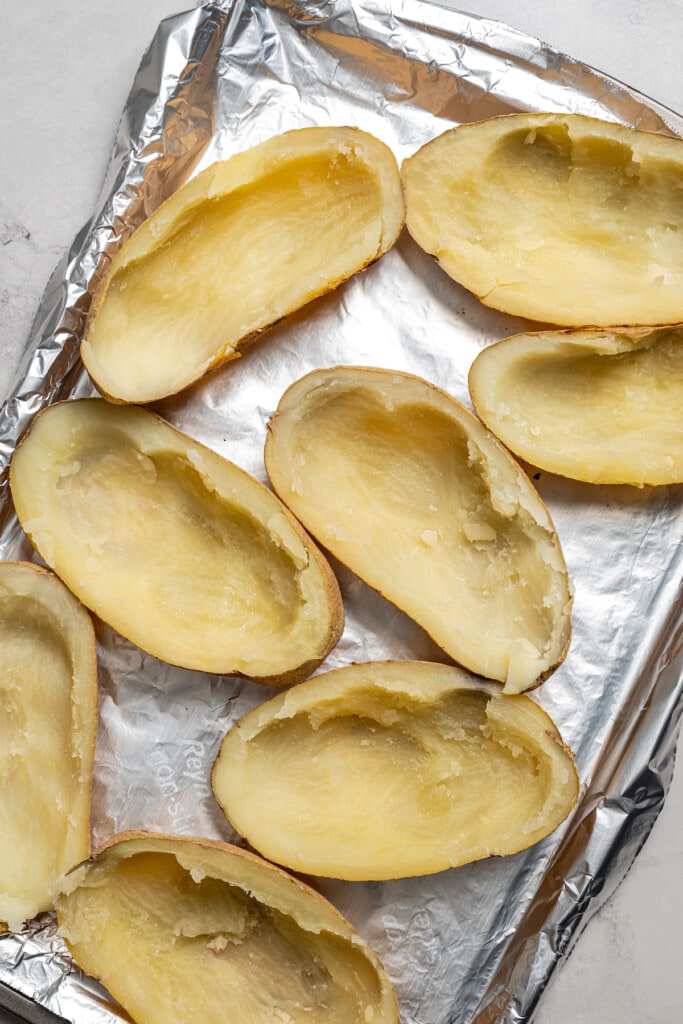 Hollowed-out baked potato halves on a foil-lined baking sheet.