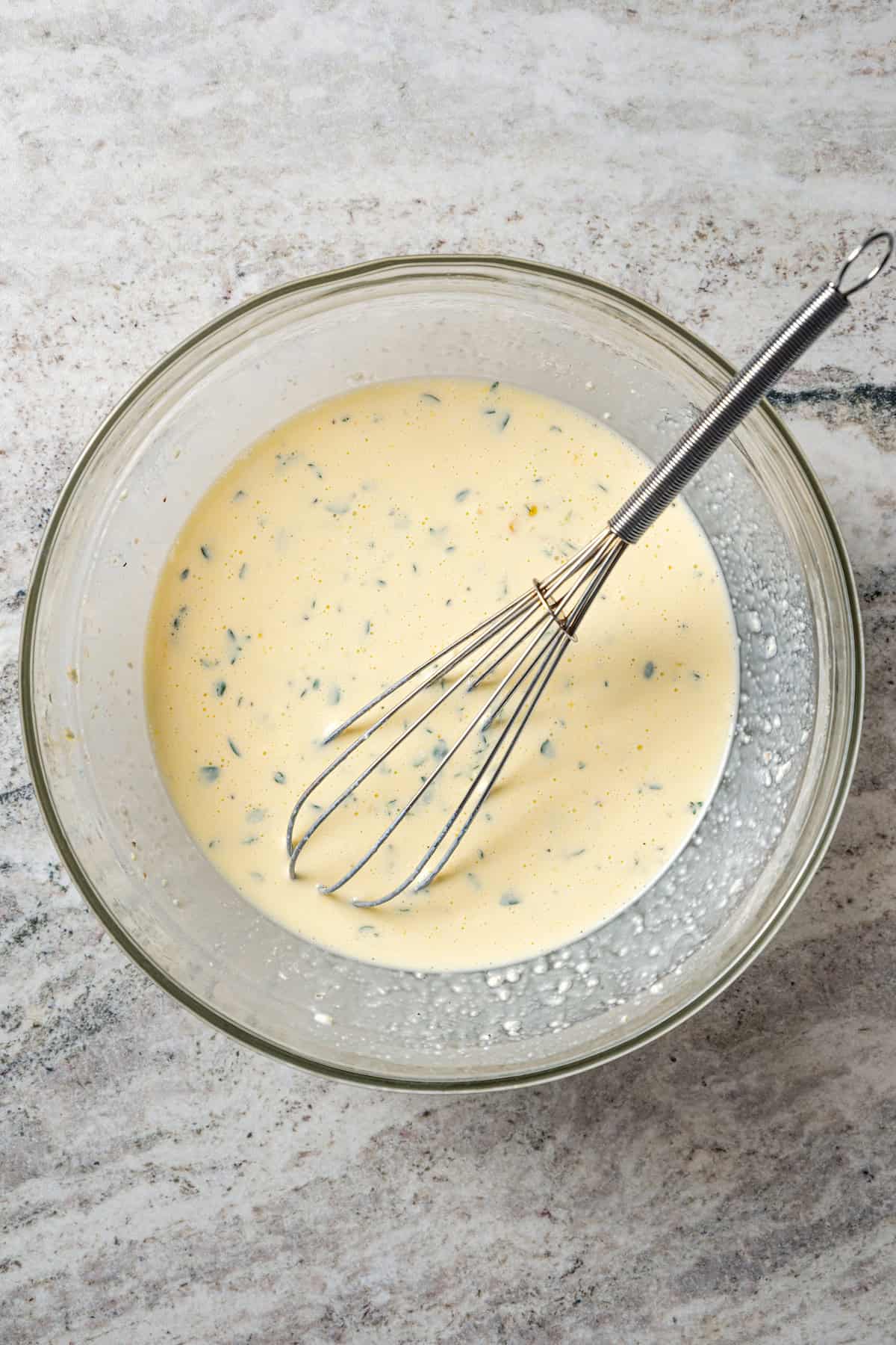 Savory custard in a glass bowl with a whisk.