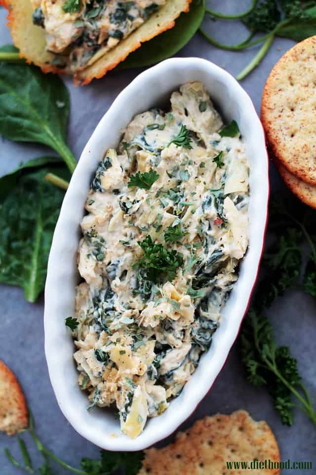 A oval shaped white bowl filled with spinach artichoke dip