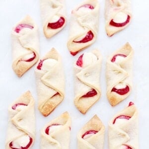 Several pastries filled with strawberry jam and soft sweetened cream cheese are arranged on a white background.