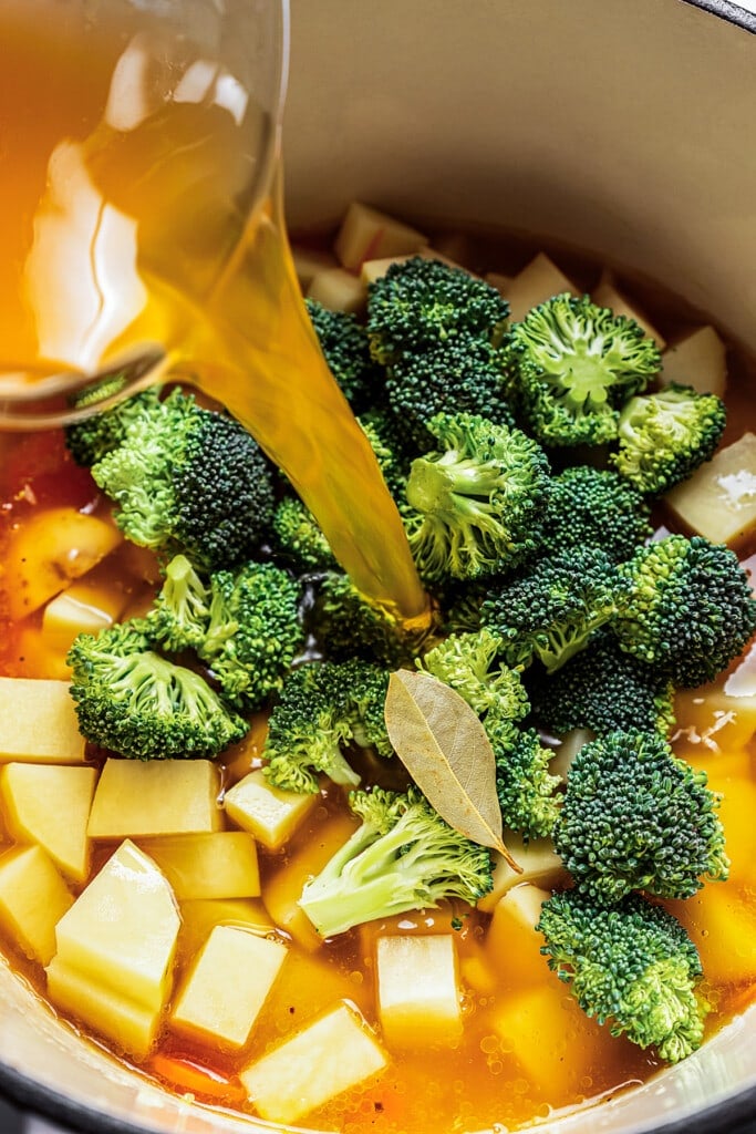 Broth is poured into a large pot with broccoli potato soup ingredients.