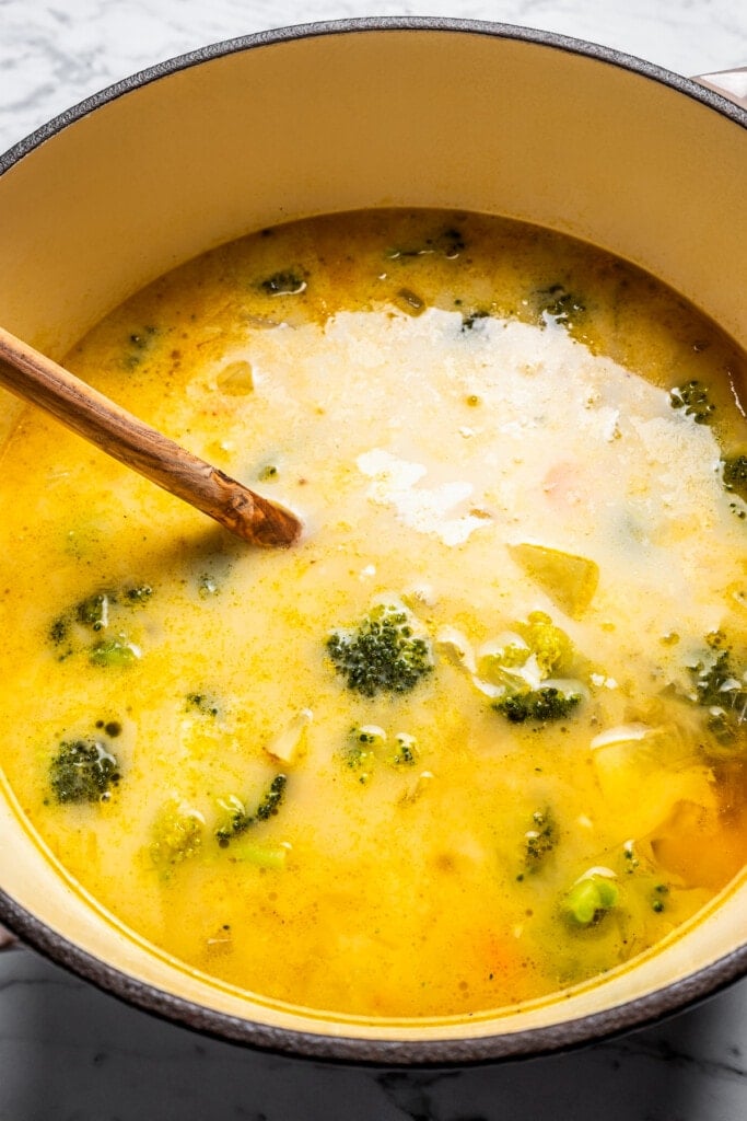 Broccoli potato soup ingredients simmering in a large pot with a wooden spoon.