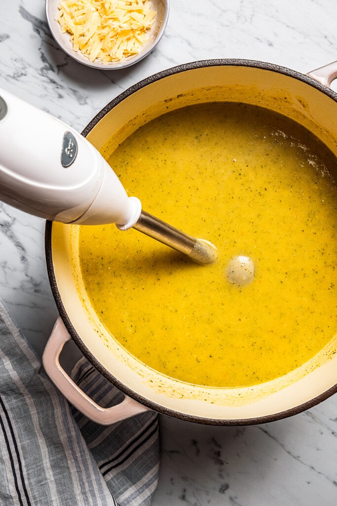 An immersion blender is used to puree broccoli potato soup in a pot.