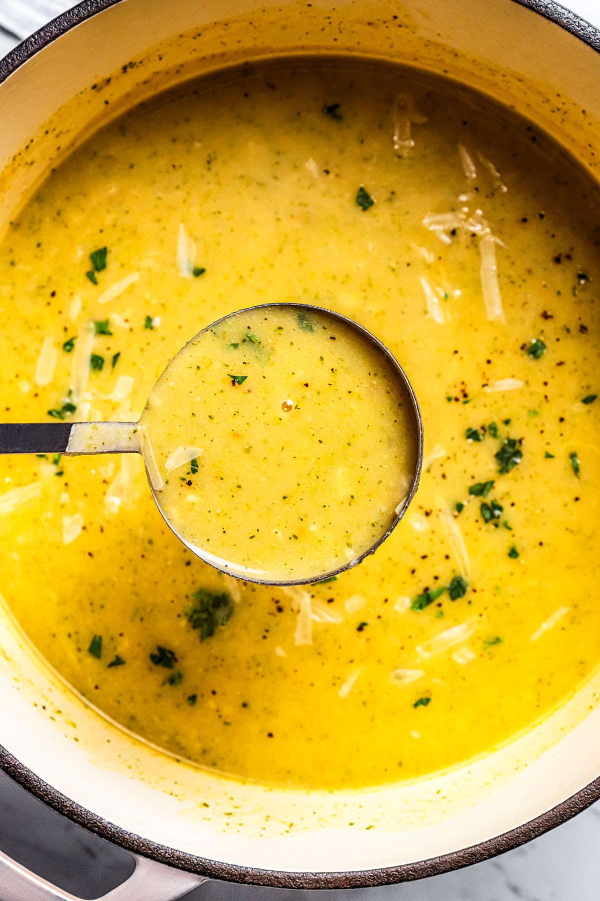 A ladle full of broccoli potato soup held over a pot.