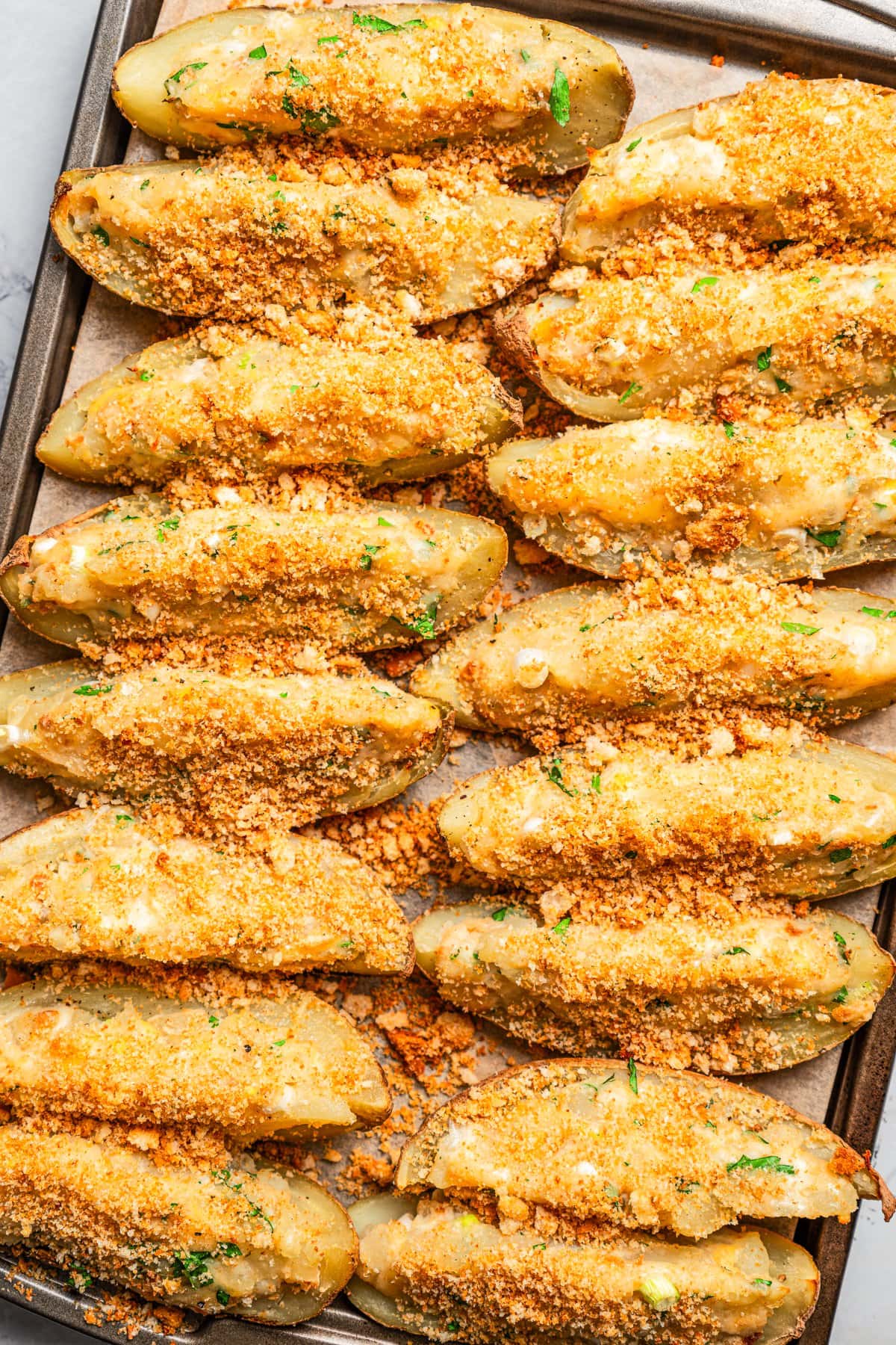 Crispy potato skins filled with mashed potato mixture, topped with crushed croutons, and arranged on a baking sheet.