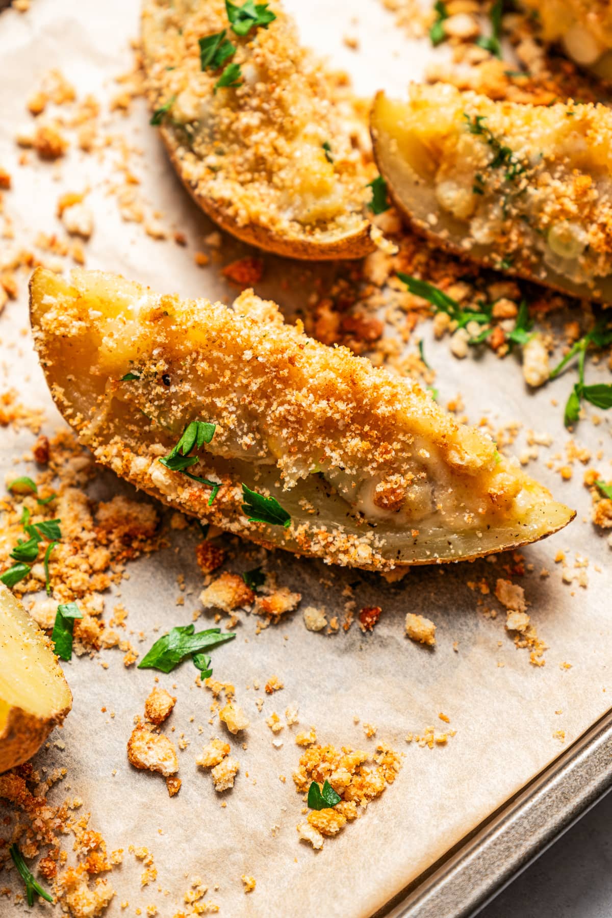 Close-up of crispy potato skins topped with crushed croutons and chopped parsley.
