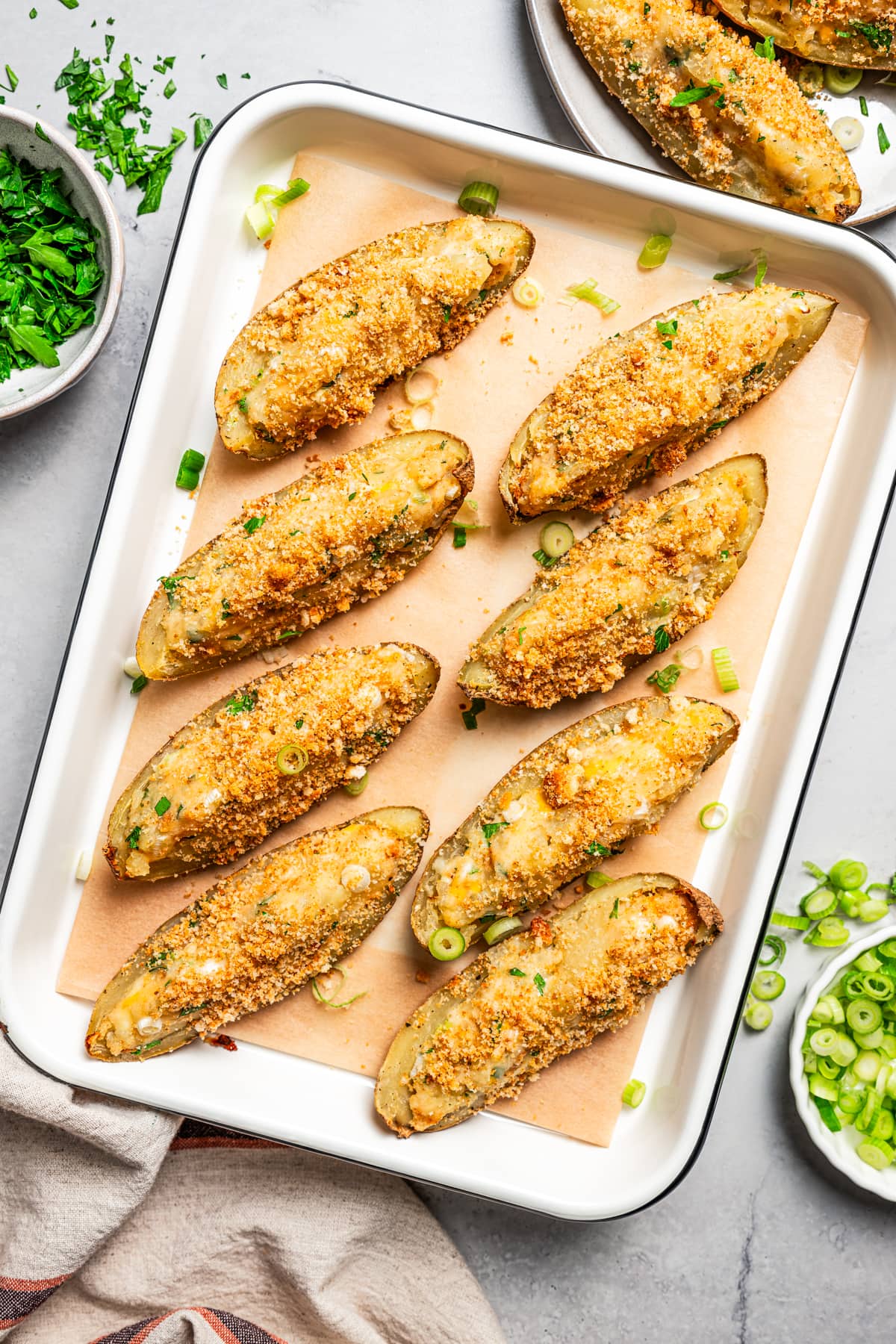 Overhead photo of crispy potato skins topped with crushed croutons and arranged on a baking sheet.