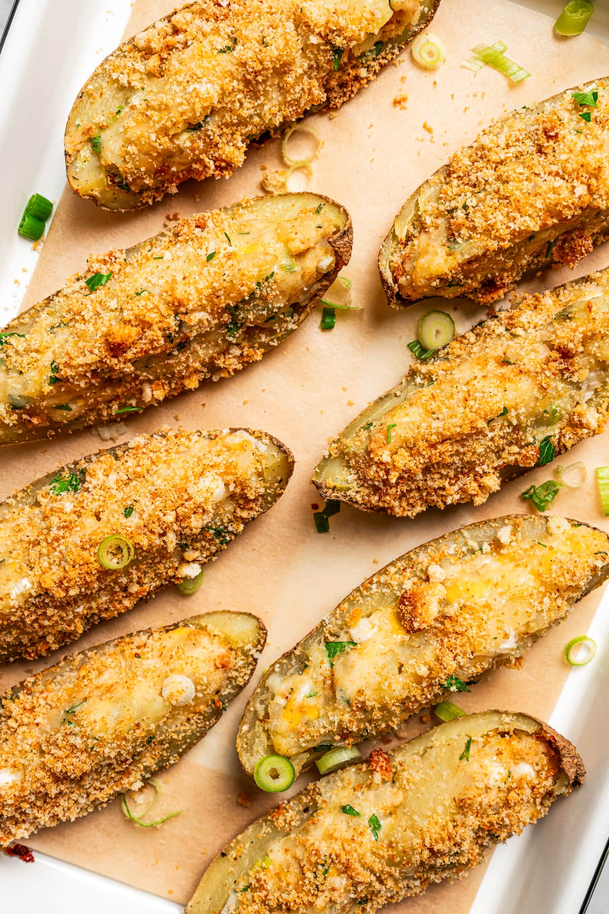 Overhead photo of crispy potato skins topped with crushed croutons and arranged on a baking sheet.
