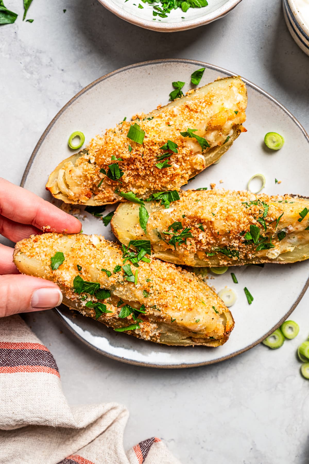 Overhead view of a hand picking up one of three crispy potato skins on a plate.