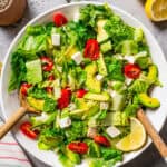 Green salad with orzo pasta, cherry tomatoes, avocado slices, and feta cheese, all served in a large bowl.