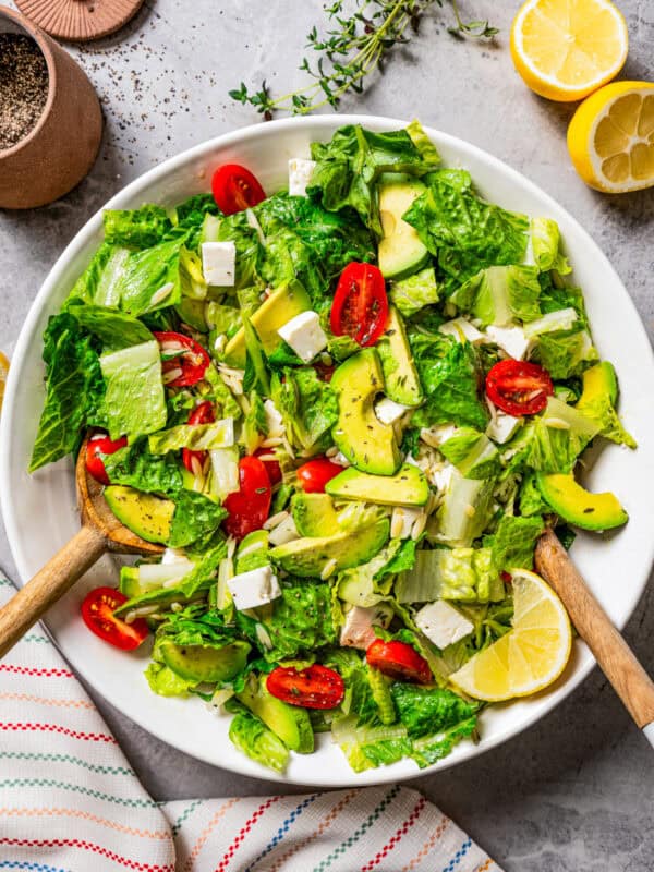 Green salad with orzo pasta, cherry tomatoes, avocado slices, and feta cheese, all served in a large bowl.