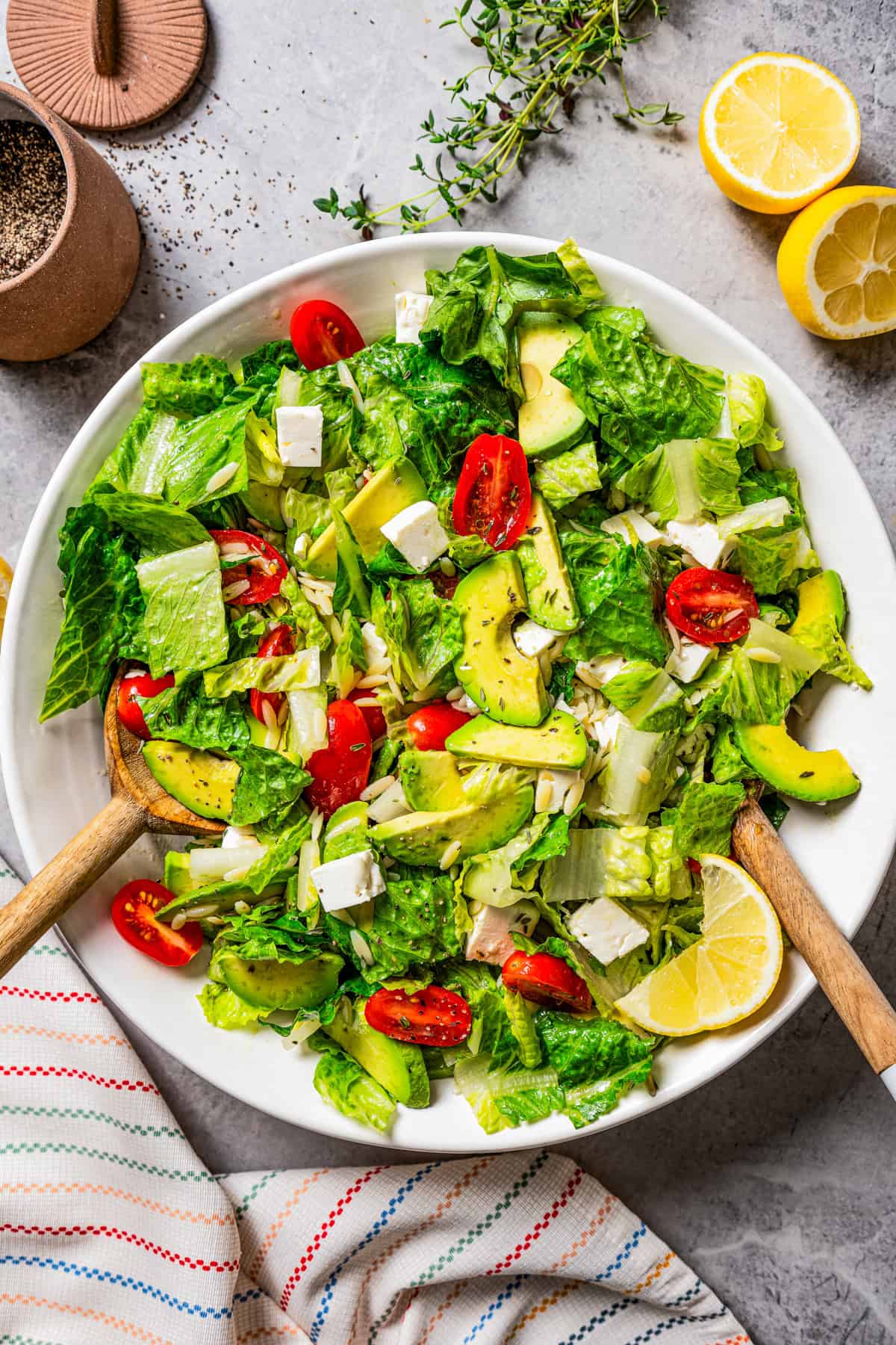 Green salad with orzo pasta, cherry tomatoes, avocado slices, and feta cheese, all served in a large bowl.