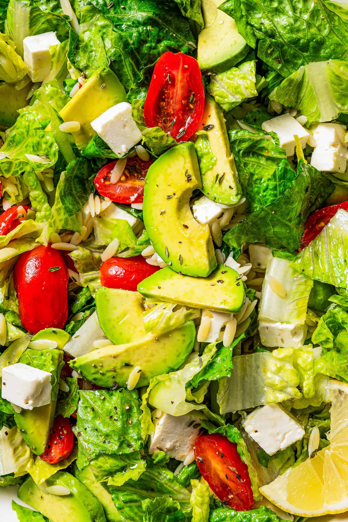 Close-up image of chopped salad greens, sliced cherry tomatoes, cubes of feta cheese, and slices of avocado.