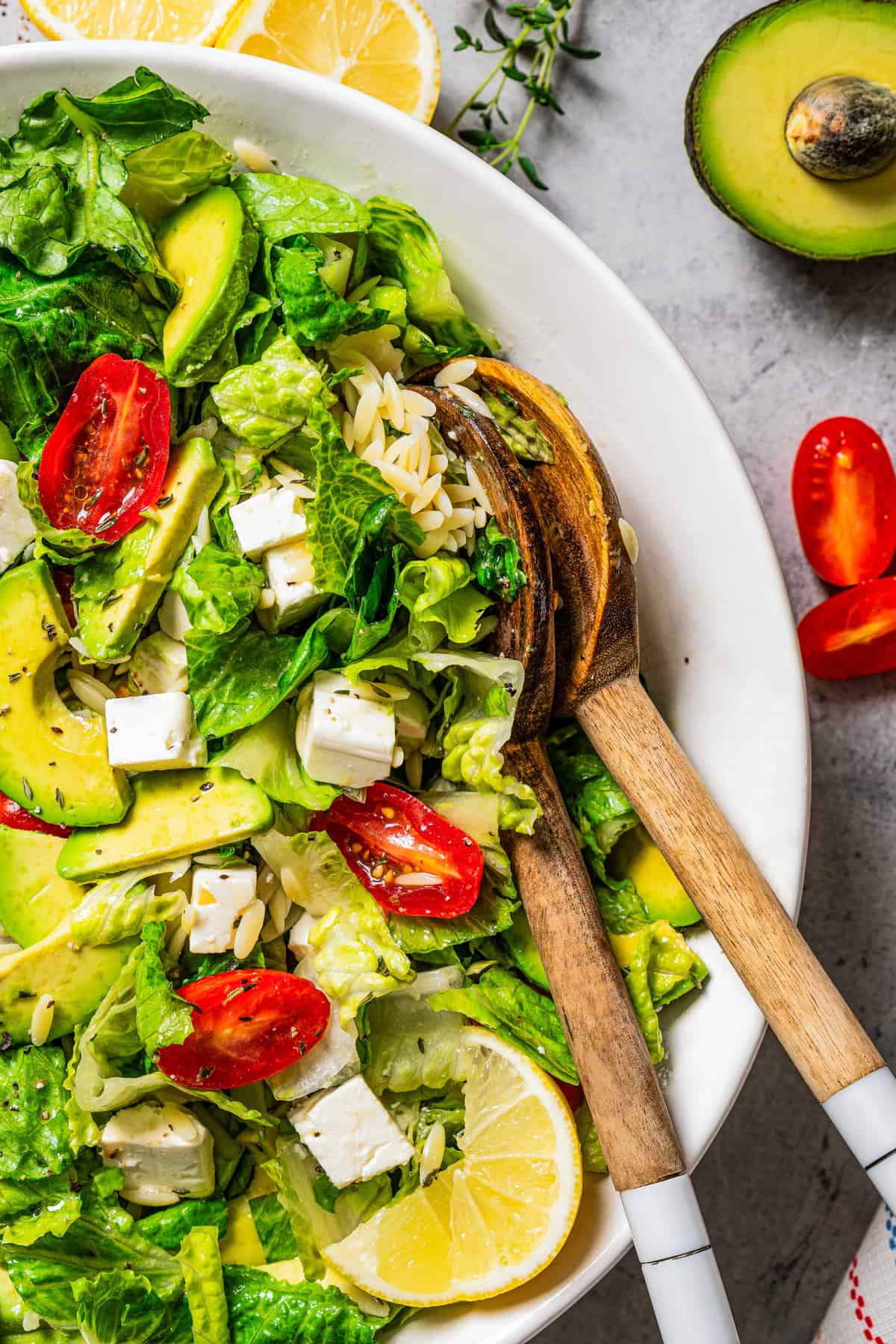 Salad greens with orzo and feta in a large bowl, with two wooden salad servers.