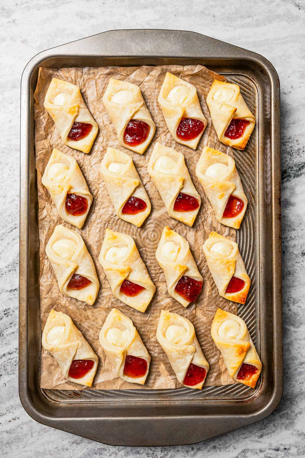 Baked kolacky cookies arranged in rows on a parchment-lined baking sheet.