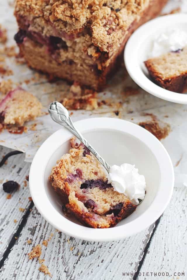 A piece of Berry Streusel Coffee Cake in a bowl with a spoon and whipped cream