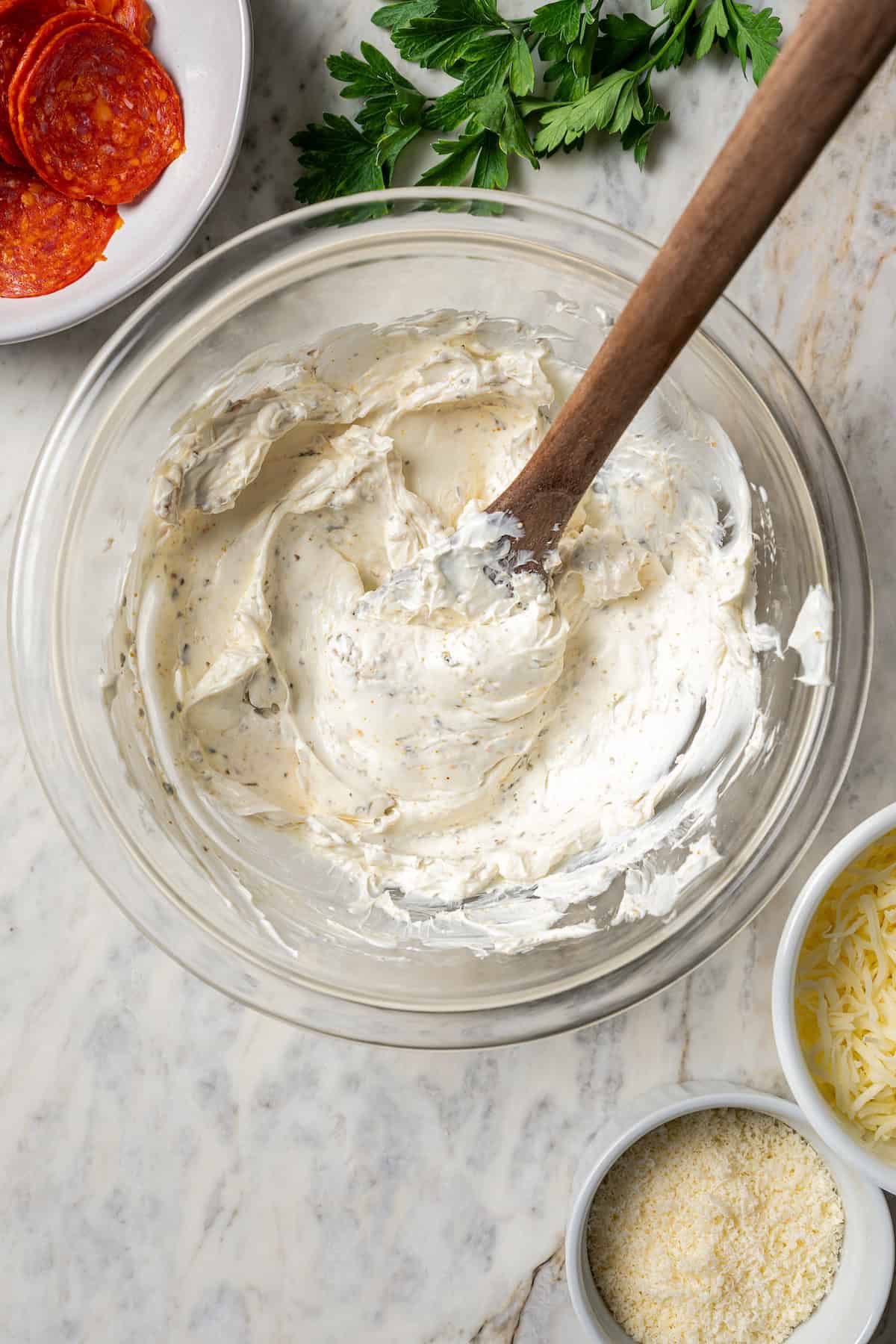 Cream cheese stirred together with seasonings in a glass bowl.