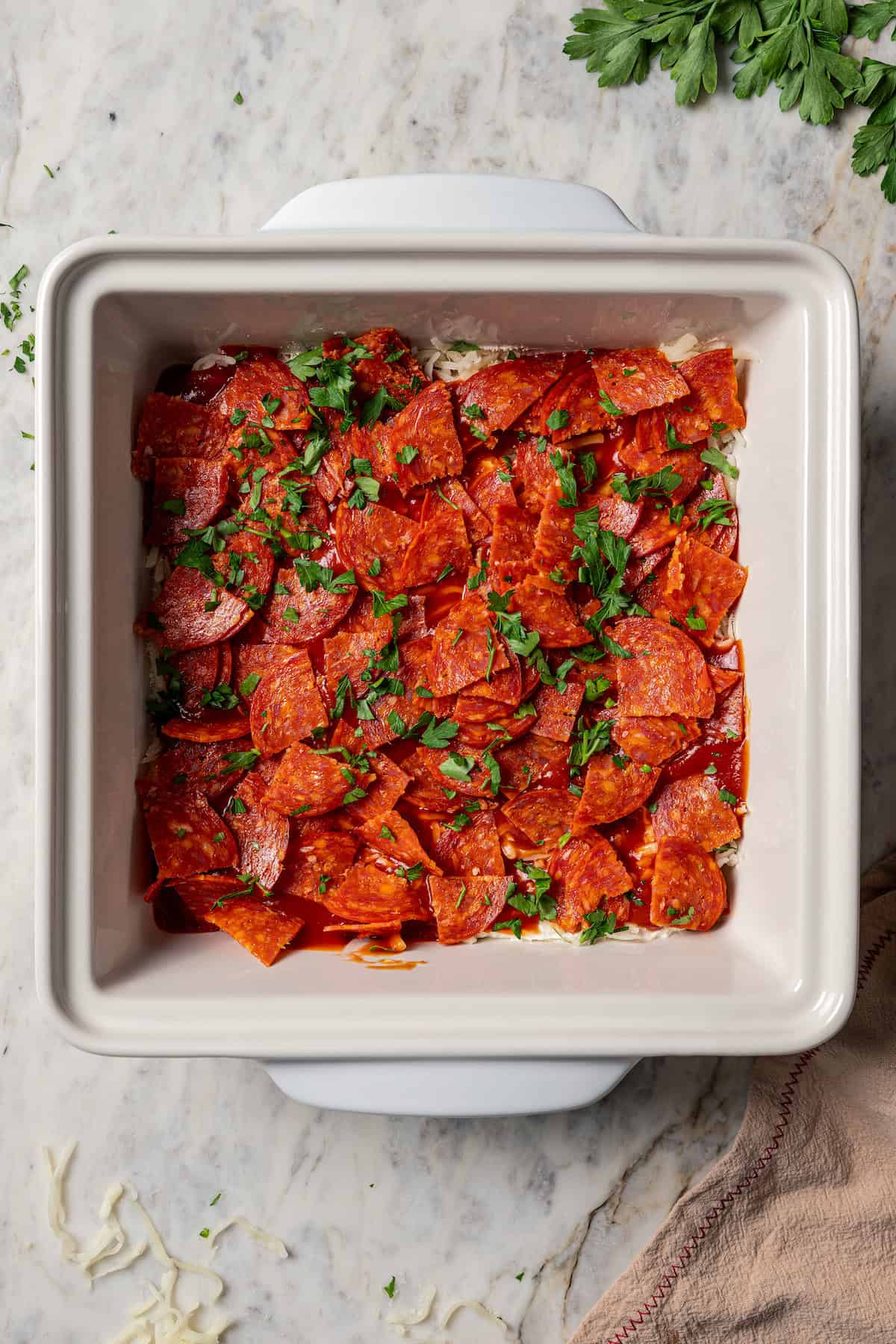 Pepperoni layered into a baking dish.