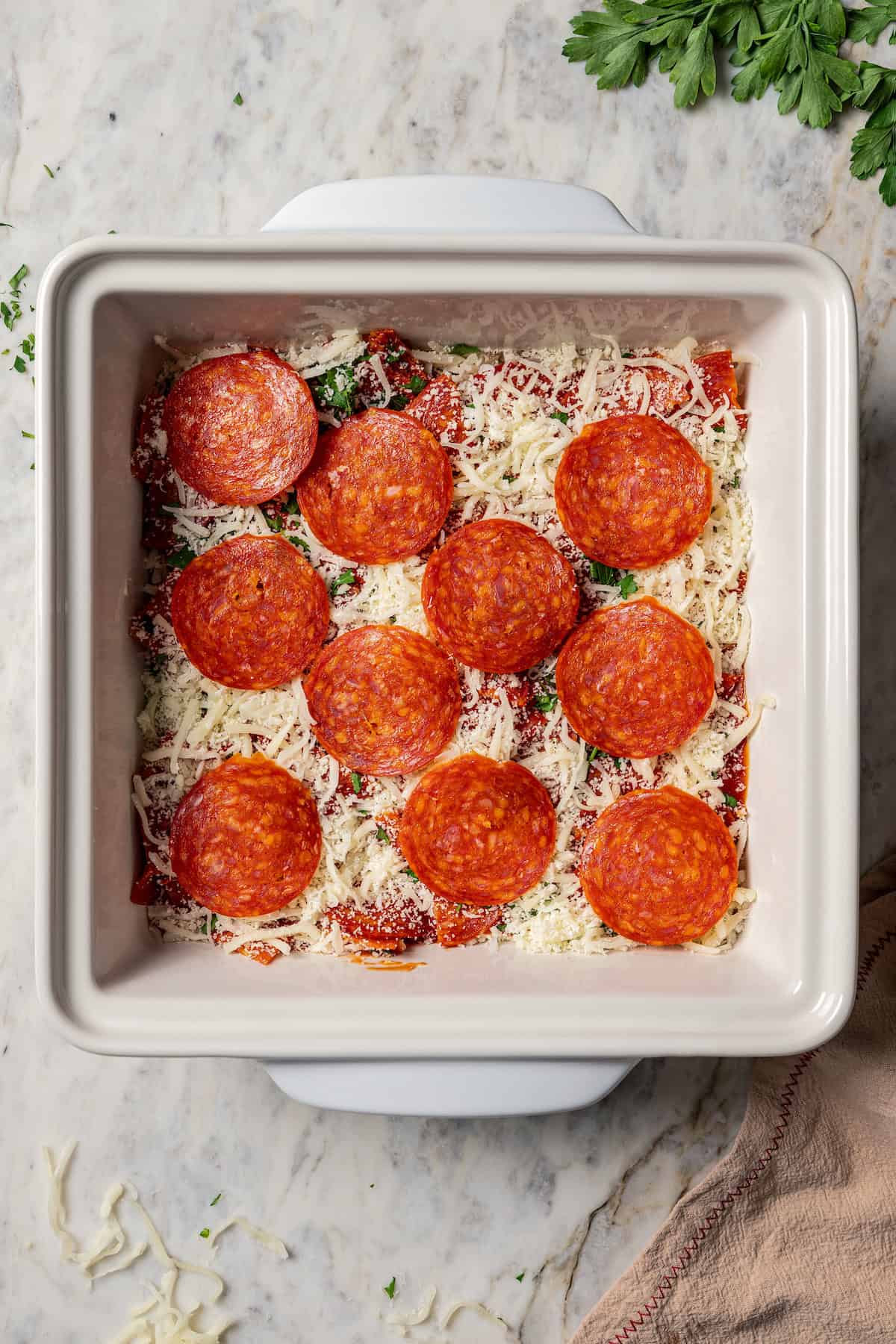 Pepperoni slices added over the rest of the pizza dip ingredients in a baking dish.