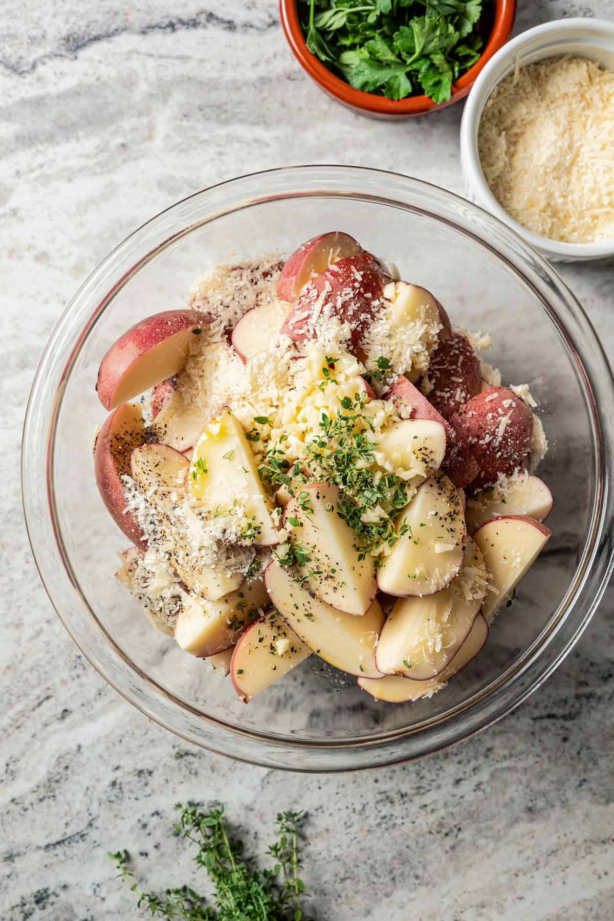 Seasonings added to potato wedges in a glass bowl.