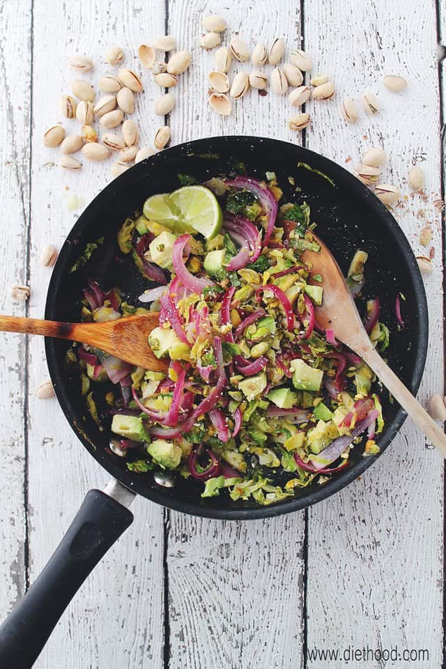 Brussels sprouts, red onion, avocado, and pistachios in a wok.