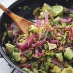 Shaved Brussels Sprouts Salad with Avocado and Pistachios in a frying pan with a wooden spoon
