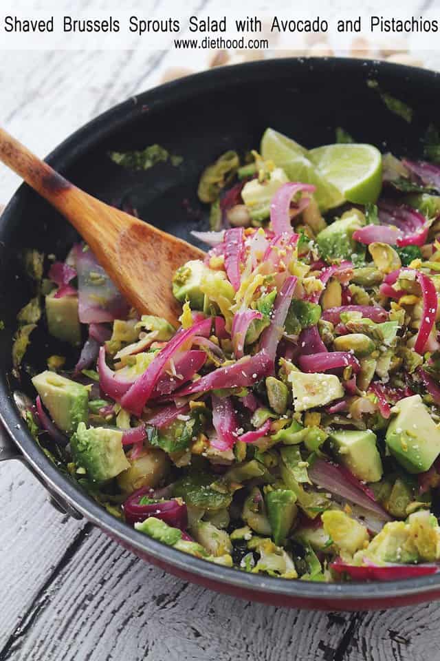 Shaved Brussels Sprouts Salad with Avocado and Pistachios in a frying pan with a wooden spoon