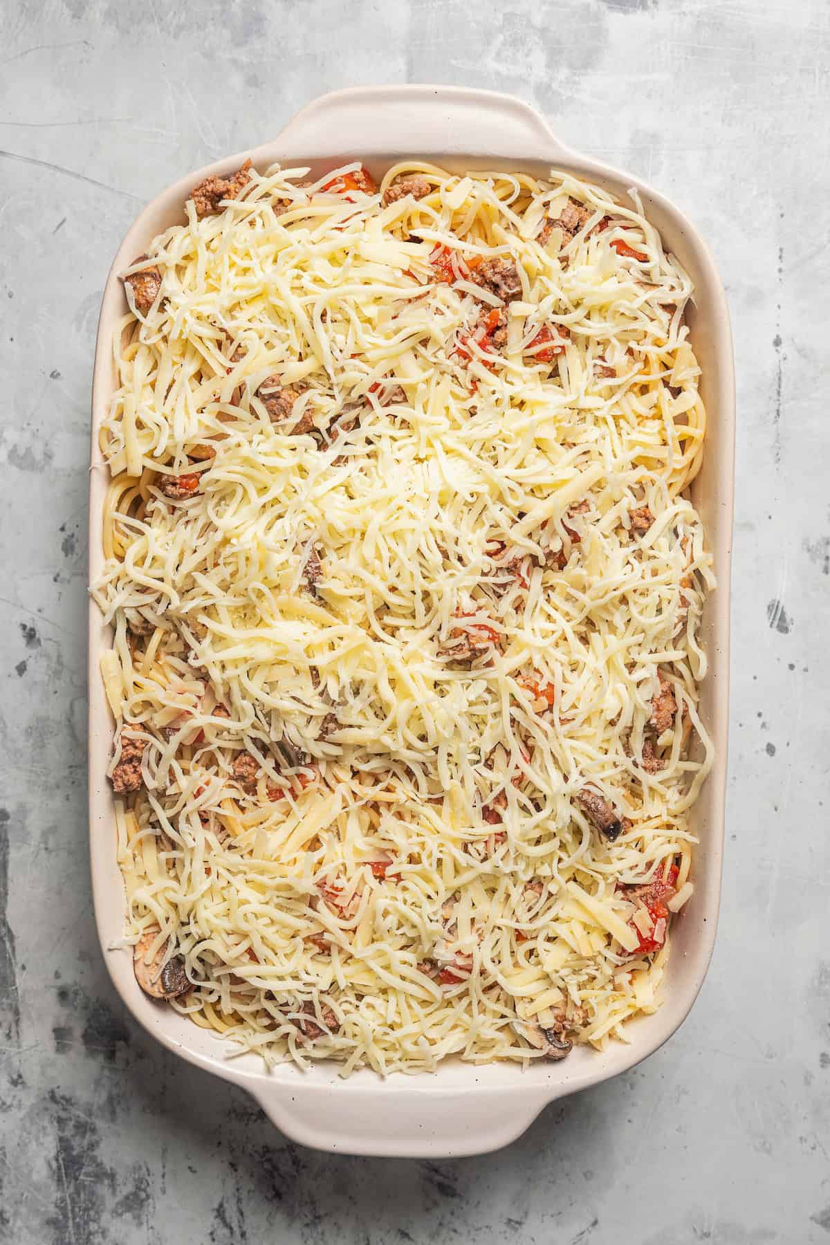Spaghetti casserole assembled inside a baking dish, topped with shredded cheese.