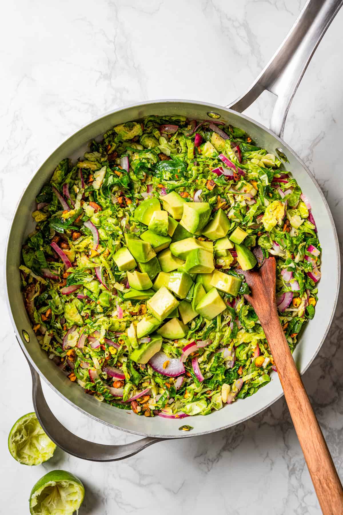 Diced avocado added to shaved Brussels sprouts salad ingredients in a skillet.