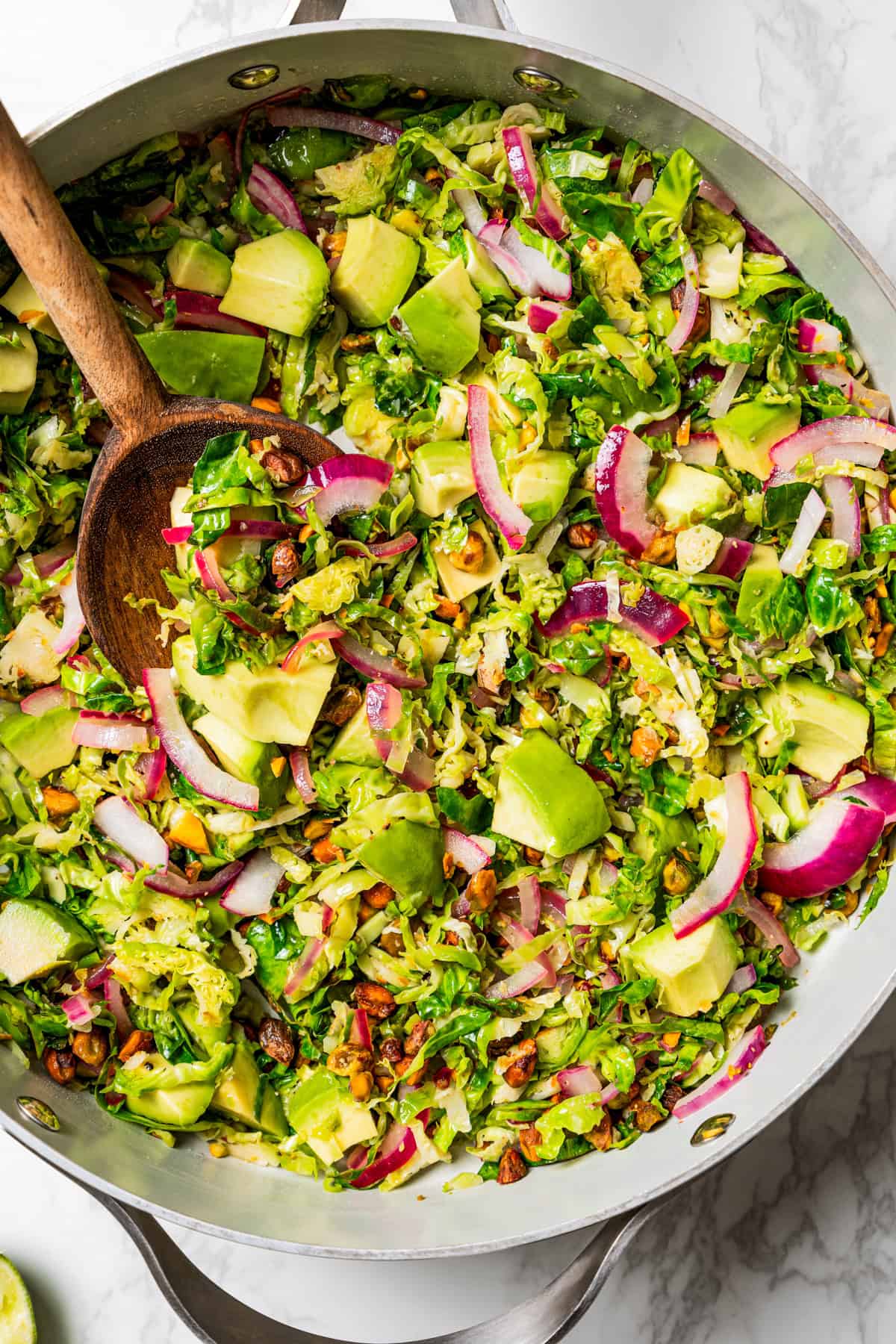 Wooden spoon stirring through shaved brussel sprouts in a pan.