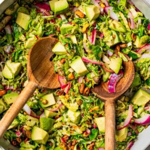 Brussels sprouts salad in a large salad bowl with two wooden salad spoons.