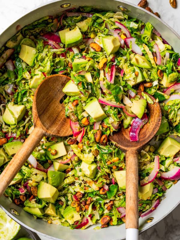 Brussels sprouts salad in a large salad bowl with two wooden salad spoons.