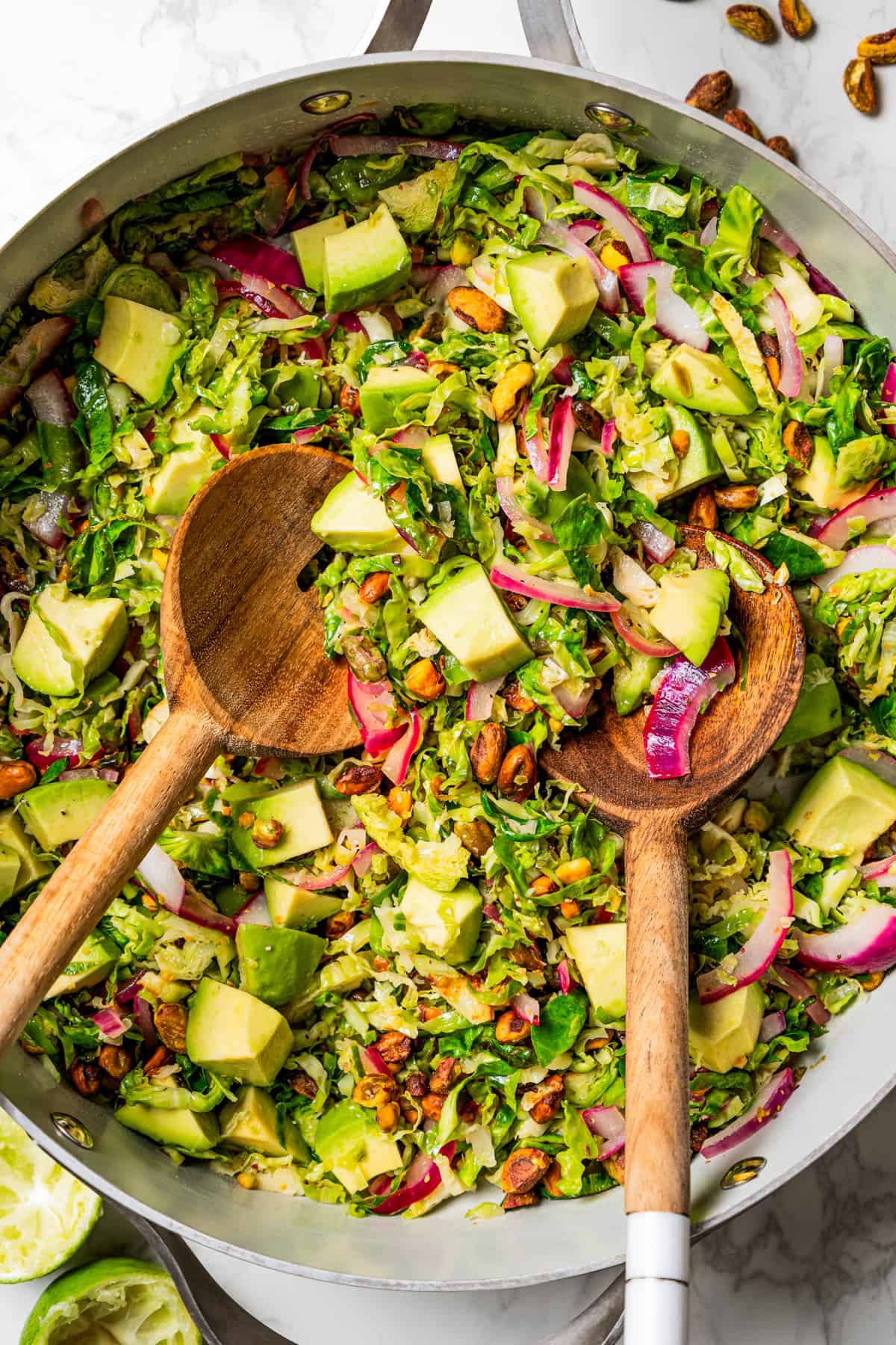 Brussels sprouts salad in a large salad bowl with two wooden salad spoons.