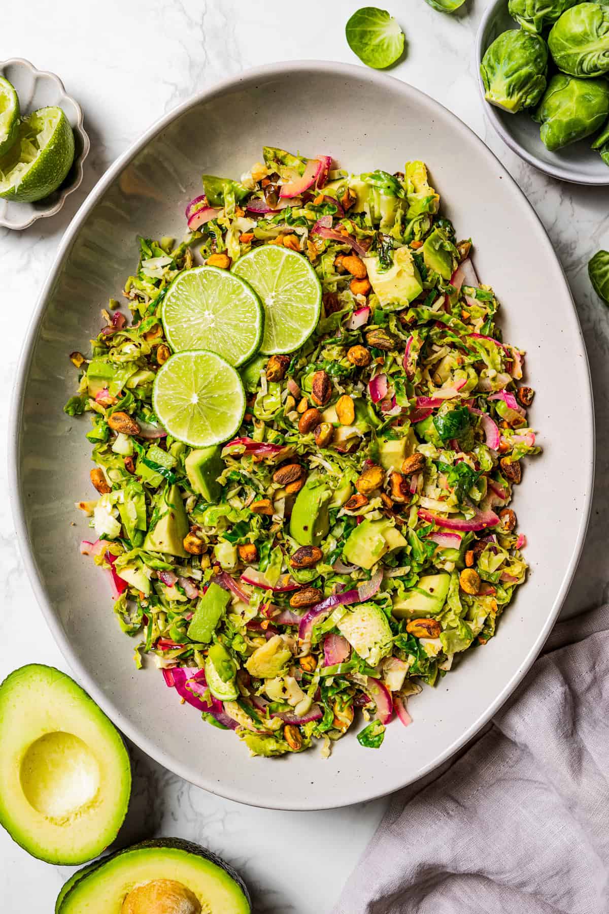 Overhead image of a shaved Brussels sprouts salad on a large platter, garnished with lime slices.