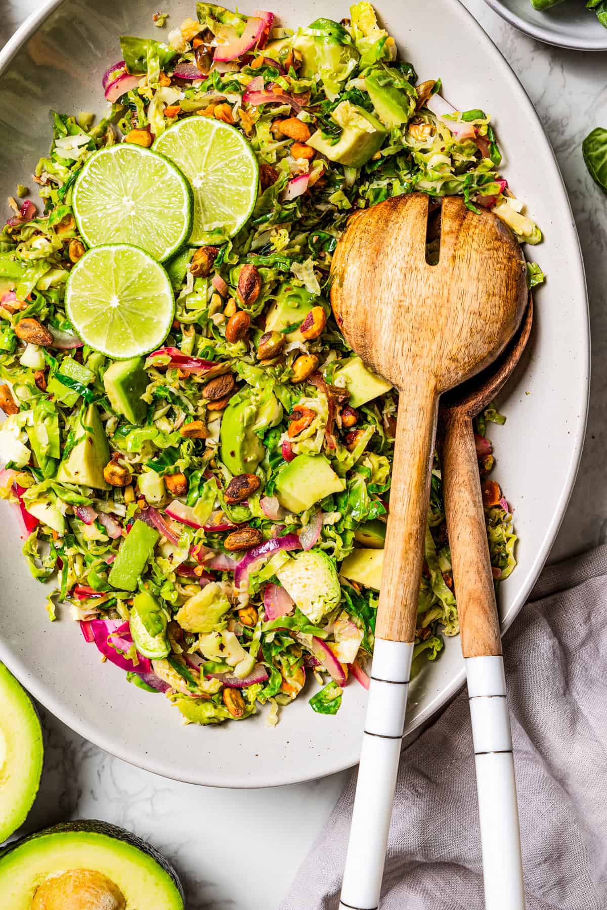 Brussels sprouts salad on a large platter with two salad spoons, garnished with lime slices.