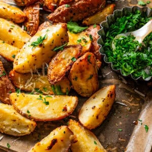 Garlic parmesan roasted potatoes next to a small bowl of parsley on a baking sheet.