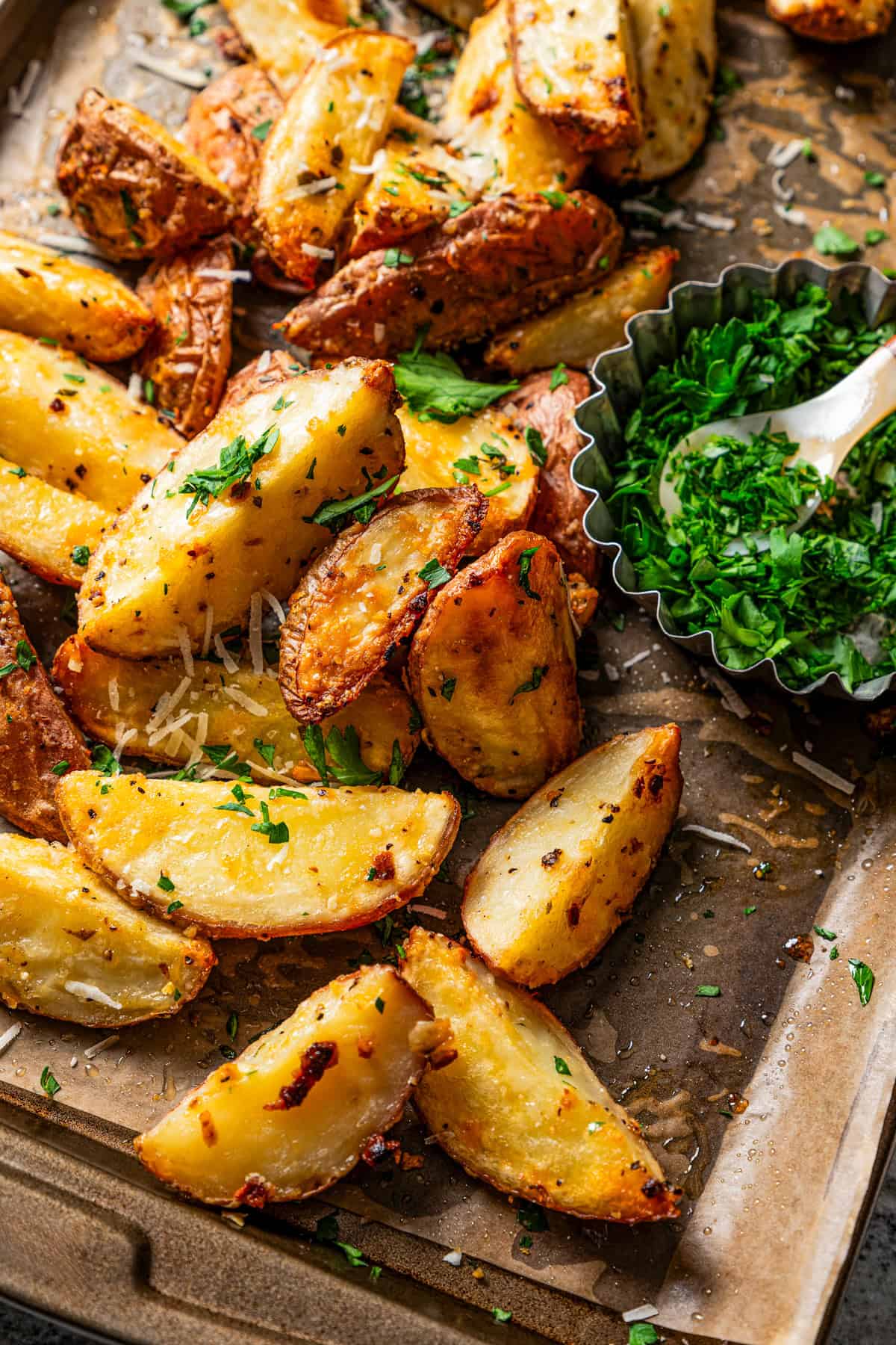 Garlic parmesan roasted potatoes next to a small bowl of parsley on a baking sheet.