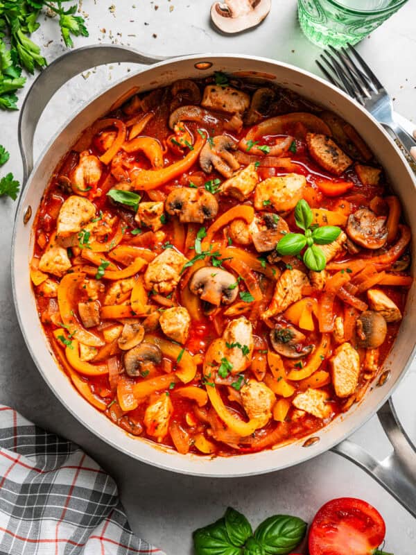 Overhead image of cooked cubed chicken pieces tossed with mushrooms, onions, and bell peppers in a pan.