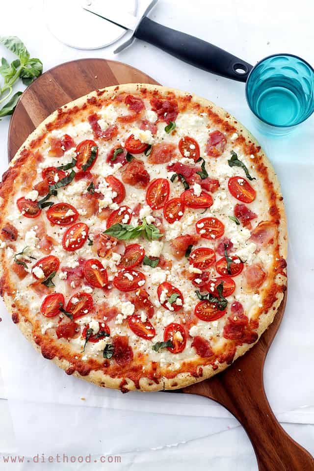Bacon, Goat Cheese and Tomato Pizza on a brown cutting board