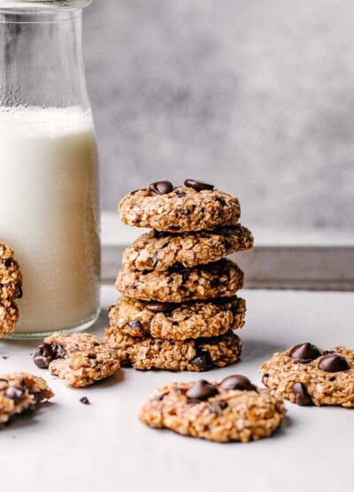 banana oats chocolate chip cookies stacked next to a milk jub