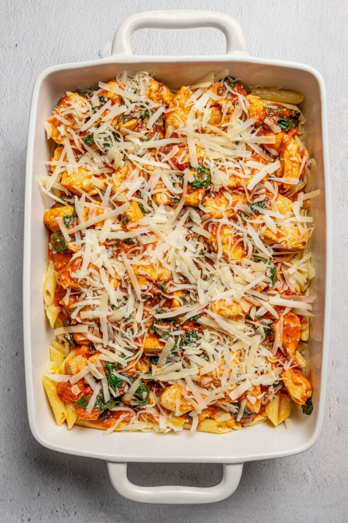 Shredded cheese added over top chicken pasta in a casserole dish.