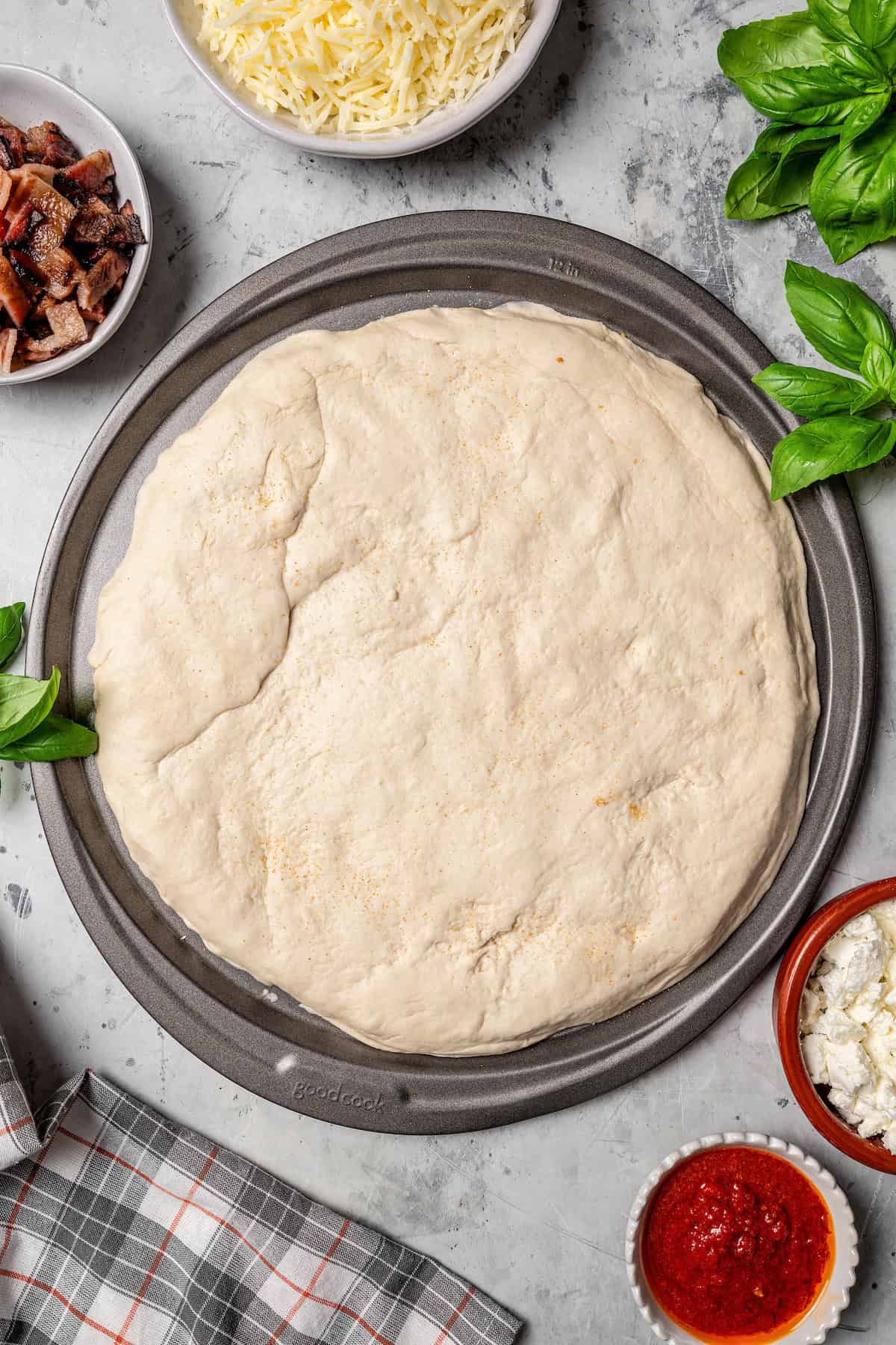 Pizza dough pressed out into a round crust inside a pizza pan.