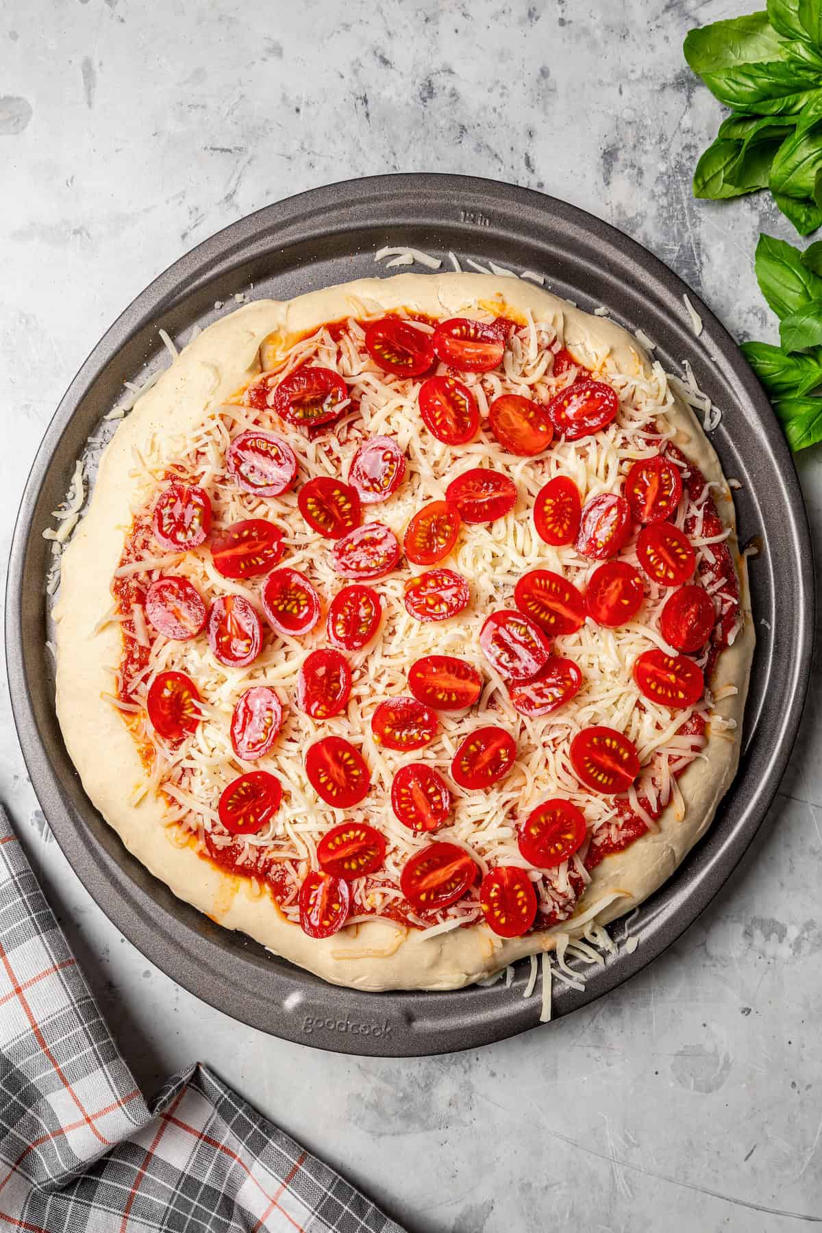 Pizza crust topped with sauce, shredded cheese, and sliced grape tomatoes.