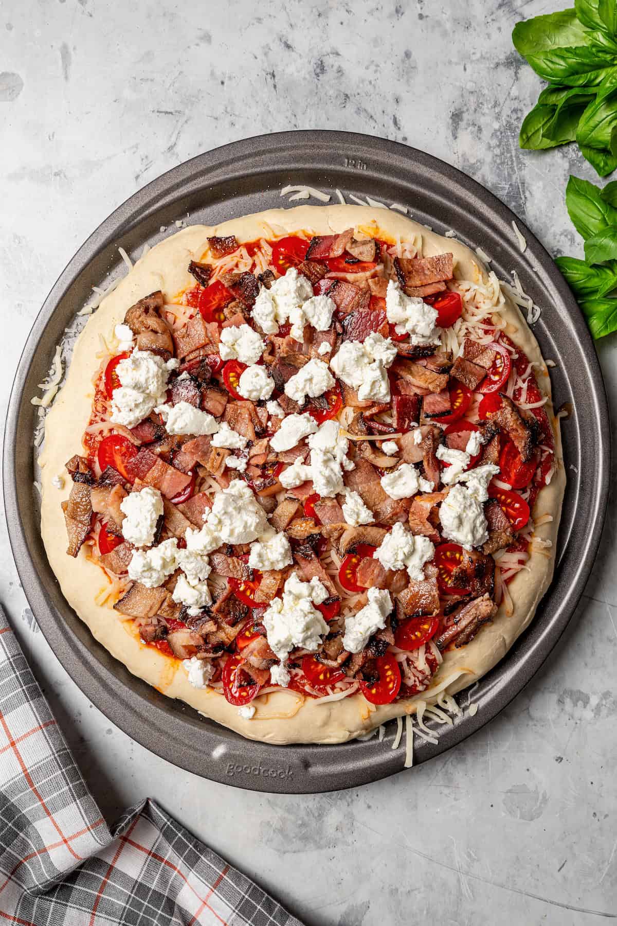 Pizza crust topped with sauce, shredded cheese, sliced grape tomatoes, bacon, and goat cheese.
