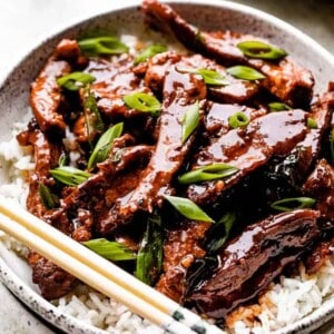 Mongolian beef served over rice on a white plate with chopsticks.