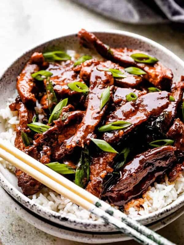 Mongolian beef served over rice on a white plate with chopsticks.