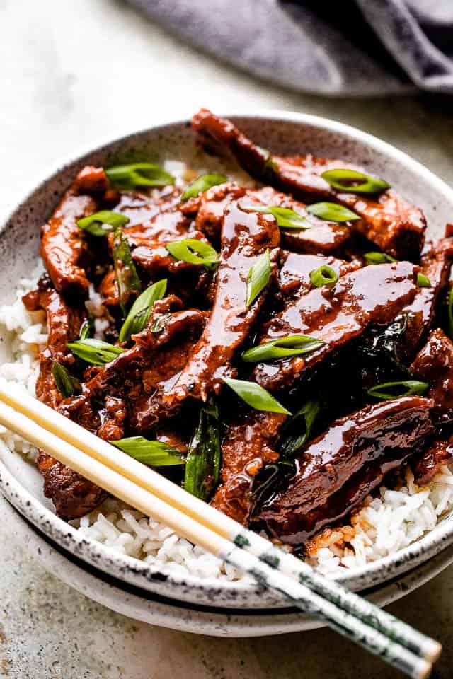 Mongolian beef served over rice on a white plate with chopsticks.