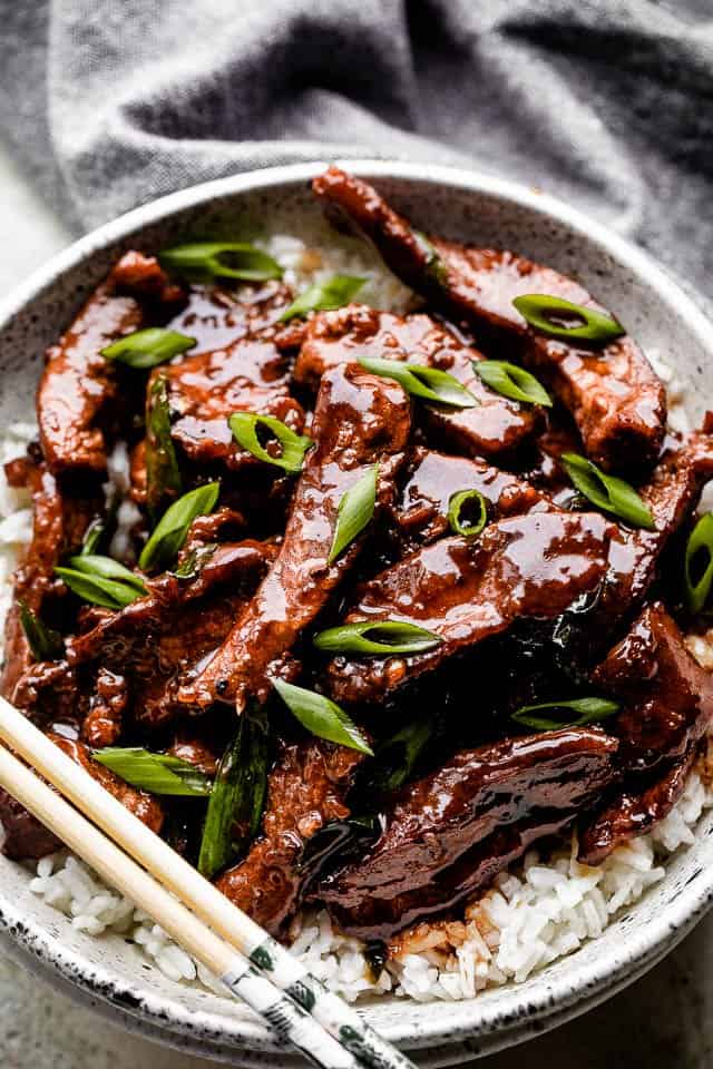 Mongolian beef served over rice on a white plate with chopsticks.